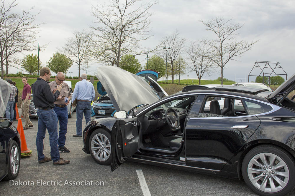 People standing and talking by electric vehicles.
